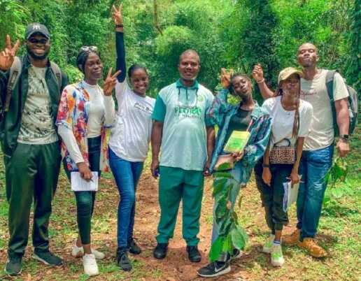 7 young people in casual clothes holding clipboards and laughing. jungle behind them