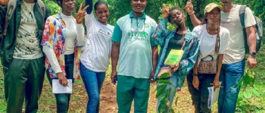 7 young people in casual clothes holding clipboards and laughing. jungle behind them