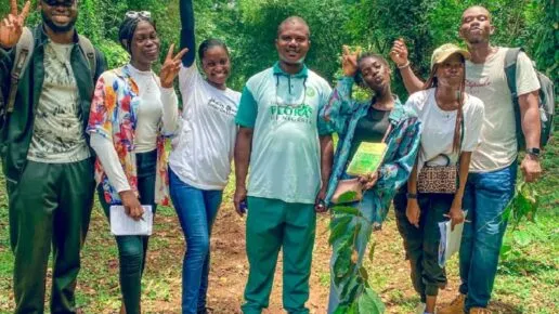 7 young people in casual clothes holding clipboards and laughing. jungle behind them
