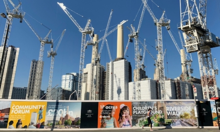 Many cranes across the skyline standing behind construction work and a wall with colourful posters on