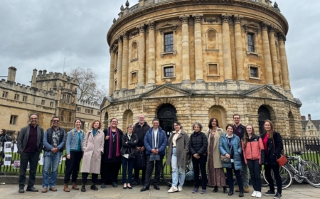 A group of men and women pose for a photo on an overcast day infront of the sheldonian building in Oxford